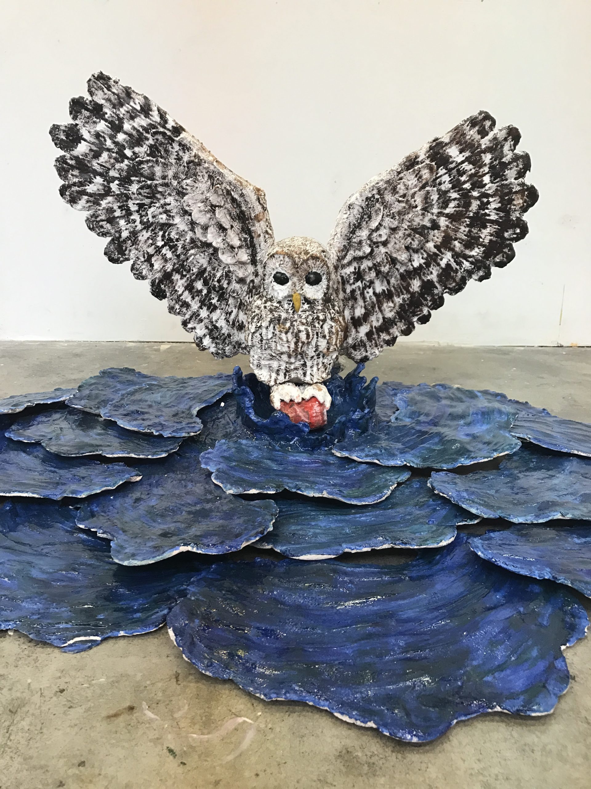 Ceramic sculpture of an owl picking a can out of a rippled lake